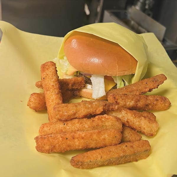 A burger wrapped in yellow paper with a side of crispy fried zucchini sticks.