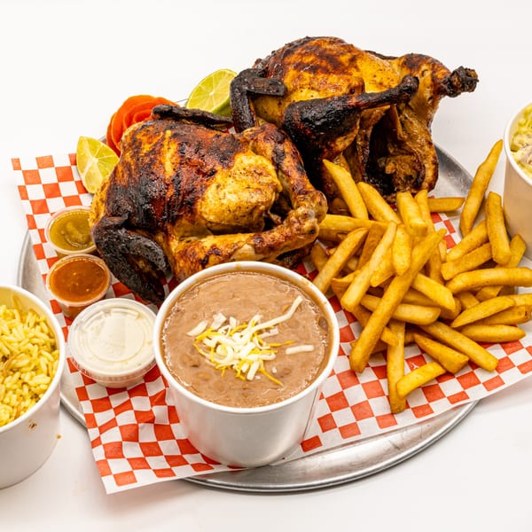 Two whole roasted chickens, fries, beans, rice, and sauces on a red and white checkered tray.