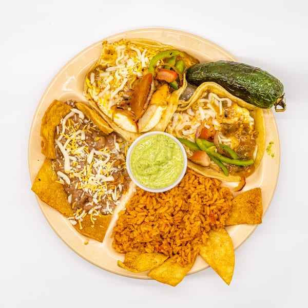A platter of tacos, rice, beans, tortilla chips, guacamole, and a whole roasted pepper.