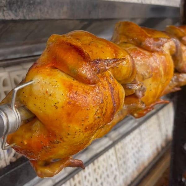 Golden-brown rotisserie chickens cooking on a spit at Neighborhood Pizzeria Y Pollo.