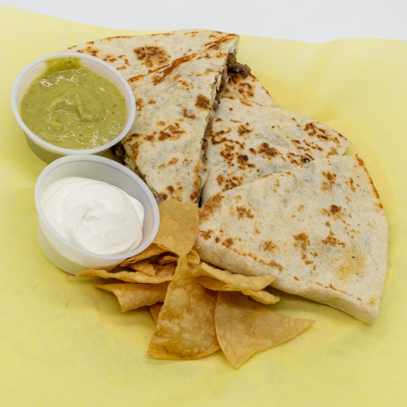 Quesadillas with guacamole, sour cream, and tortilla chips on yellow paper.