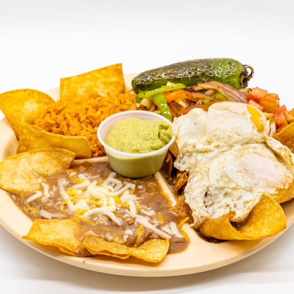 A plate of Mexican food with fried eggs, rice, beans, tortilla chips, guacamole, and a large pepper.